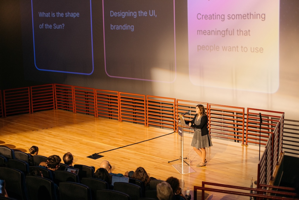 Leah Spalding presents on an IMAX theatre stage.